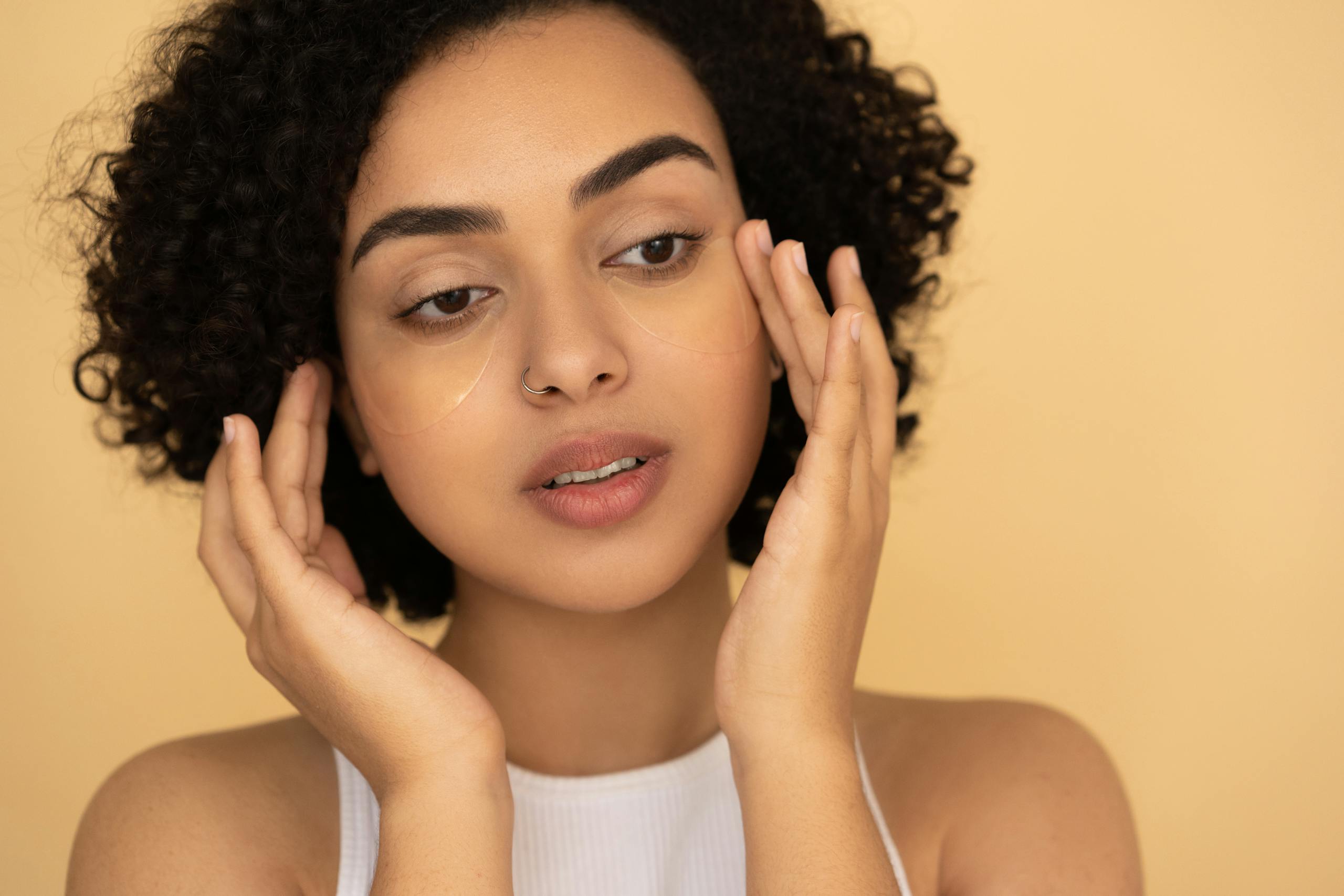 Close-up of a woman applying under-eye mask in a studio setting, focusing on skincare and wellness.