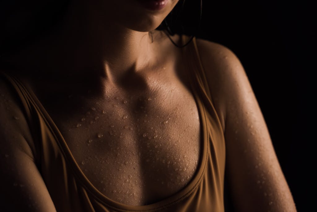 Close-up of a woman's wet skin with water droplets, set against a dark background.