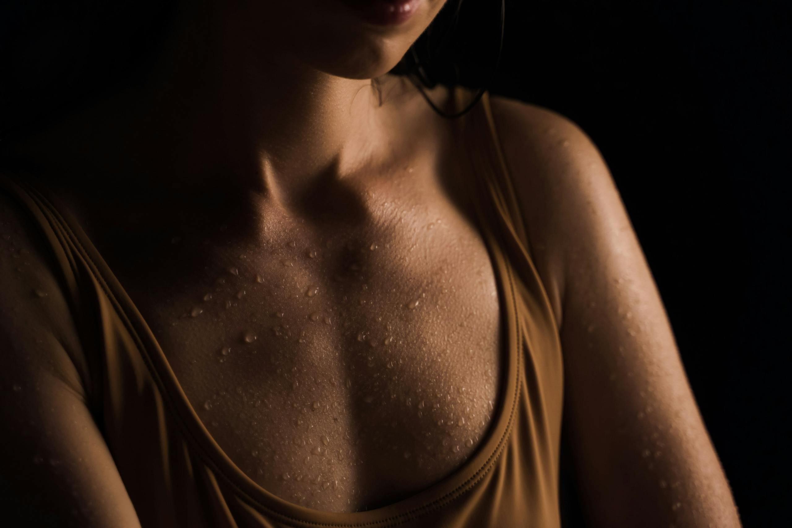 Close-up of a woman's wet skin with water droplets, set against a dark background.